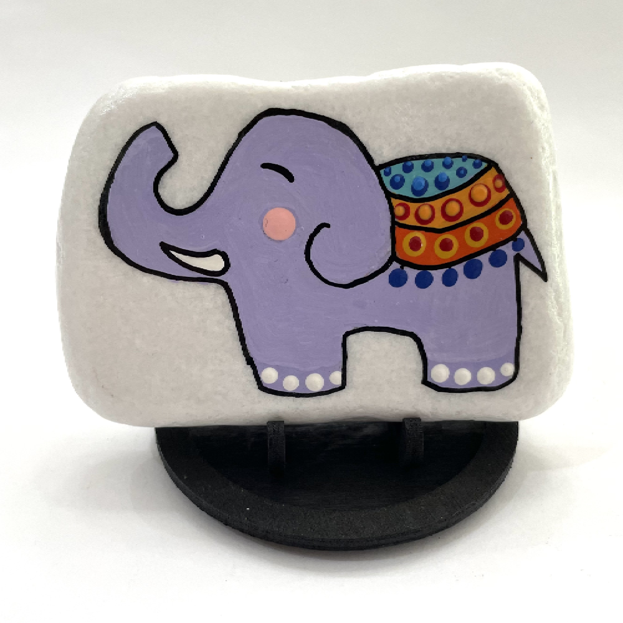 Hand-painted purple elephant on a white rock with a decorative blanket, displayed on a black stand Hand painted purple elephant on a white rock with a decorative blanket, displayed on a black stand